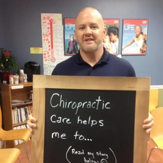 Dr. Chris Thornell holding a chalkboard that reads Chiropractic care helps me to
